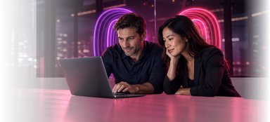 Two traders smiling while reviewing the EDGE platform on a laptop