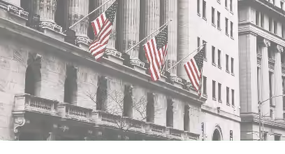 Fachada neoclássica de um edifício de bolsa de valores com bandeiras americanas, representando o mercado de ações
